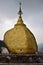 Pilgrims praying and pasting gold foils together onto golden rock at the Kyaiktiyo Pagoda, Myanmar with row of small bells