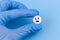 A pill with a sad emoticon in a hand in a medical glove on a blue background. Health care