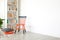 Pillows next to orange and black chair in white room interior with copy space on empty wall