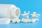 Pills spilling out from white container. White medical pills spilling out of pills bottle, blue background