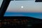 Pilots view out of the cockpit window toward sunset sky with the moon rising high