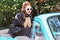 Pin-up girl wearing vintage clothes, sitting on old car hood.