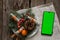 Pine branch twisted into a roll dollars and a phone with a green screen on a wooden table, christmas decoration