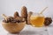 Pine nuts in a bowl and honey in a glass pot on a light background next to cedar cones