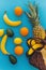 pineapple and bananas,oranges,lemons,avocado falling from stylish straw bag on blue trendy paper background. summer multi fruit c