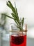 Pineapple blackberry cocktail in shots with a garnish of frozen blackberries and a sprig of rosemary on a gray-white background