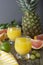 Pineapple cocktail or juice in glass jar bottle with straws and fruits on background - pineapple, oranges, grapefruit, lime and