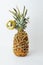 Pineapple decorated like a Christmas tree. Gold beads garland. Golden shining reflective disco ball. White background