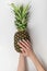 Pineapple in female hands. Summer manicure on short nails. White background. Vertical frame
