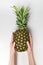 Pineapple in female hands, white background. Summer manicure. Vertical frame