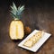 Pineapple fruit cut half, quarter and wedges and displayed on white plate and wooden background. Square Composition. Juicy organi