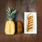Pineapple fruit cut half, quarter and wedges and displayed on white plate and wooden background. Square Composition. Juicy organi
