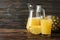 Pineapple, glass jug and glass with juice on wooden background