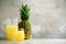 Pineapple juice in glassware and whole pineapple fruit on gray background. Copy space, sunlight effect. Summer, holiday