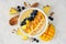 Pineapple, mango smoothie bowl with coconut, bananas, blueberries and granola, above view on a bright background