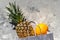 Pineapple and orange in a white paper bag on a gray non-uniform background. Vitamin-rich tropical fruits. Healthy diet