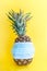 Pineapple wearing surgical medical mask on yellow background. Coronavirus, allergy, safety summer concept