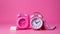 A pink alarm clock and a pink phone on a pink background