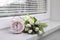 Pink alarm clock and wonderful tulips on window sill indoors. Spring atmosphere
