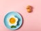 Pink background with egg in a flower shaped bowl and blue plate with broken egg shells and kitchen utensils