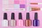 On a pink background, multicolored nail polishes are located in the bottom row, eye shadows and brushes are on top