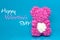 Pink bear, toy with white heart on a blue background with the words happy valentine`s day.