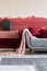 Pink blanket and burgundy pillows on grey sofa in trendy living room interior with chest of drawers