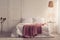 Pink blanket on white bed in minimal bedroom interior with lamp above table with plant