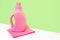 Pink bottle is standing on a pink bright cloth for cleaning against a green wall