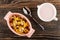 Pink bowl with corn flakes, raisin, peanut, spoon, pitcher with yogurt on wooden table. Top view