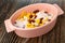 Pink bowl with corn flakes, raisin, peanut and yogurt on wooden table. Top view