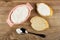Pink bowl with soft cottage cheese, sandwich with cottage cheese, slice of bread, spoon on table. Top view
