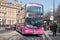 Pink branded double decker bus pulling into a bus stop to pick up passengers
