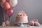 a pink cake with candles and balloons on a white cake stand on a white table with a pink teddy bear and a pink bow on it