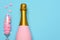 A Pink Champagne bottle and a flute with candy hearts on a blue teal background. Horizontal high angle shot with copy space