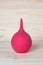 A pink clyster in shape pear with nozzle or tip on wood background. A rubber bulb syringe for douching. Medicine equipment for