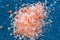 Pink coarse salt crystals on blue table. Himalaya salt. Background for advertising salty.