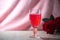 Pink collagen drink in a wine glass, placed on a wooden plate.