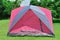 Pink color camping tent on green grass and trees behind.