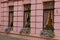 A pink concrete wall of a house with a row of three windows with curtains and flowerpots