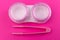 Pink container for contact lenses and tweezers on a pink background. Close-up.