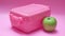 A pink container with a green apple on top of it