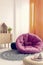 Pink cozy pouf in the middle of fashionable natural kid`s room with wooden furniture and ethno carpet on white floor