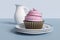 Pink cupcake on a stack of white ceramic plates with a white milk jar in the pale blue background