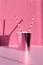 Pink disposable drink cup with straw on table against wall with shadow, closeup
