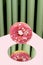 A pink donut falls on a mirror against a backdrop of green curtains