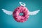 pink donut with white paper wings and nimbus on a blue background