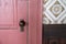 Pink door, with doorknob, next to a wall with wallpaper and a chairrail. Old fashioned style from the 1900s