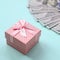 Pink dotted gift box lies near hundred dollar bills on a light blue background
