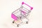 Pink empty shopping cart from the supermarket as a symbol of consumption and consumerism on light background